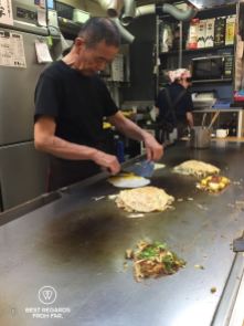 Japanese chef cooking Okonomiyaki, the savory pancakes, at Okonomi-mura, Hiroshima, Japan