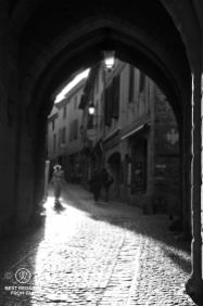 Black and white photo of a medieval gate, women walking through in a beam of sunlight.