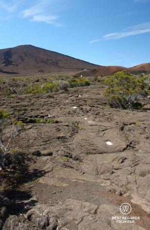 The summit of Furnace Peak on Reunion Island with the hiking path leading to it and its white trail markers on dark basalt