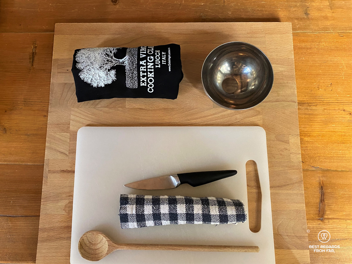 Wooden cutting board with a smaller white cutting board, a bowl, apron, knife and kitchen towel